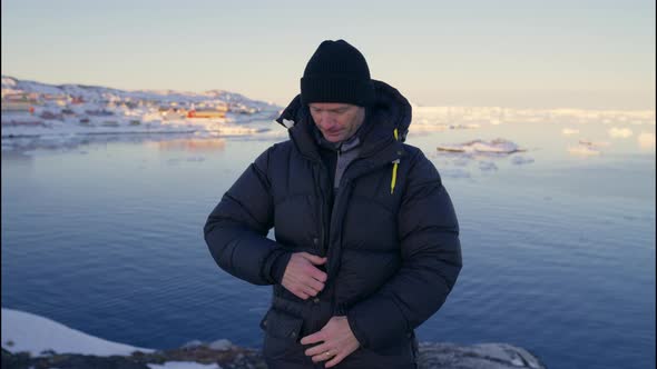 Man Zipping Up Warm Coat On Coastline Of Ilulissat Icefjord