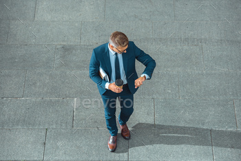 successful middle aged businessman holding coffee to go and checking wristwatch on street / Photodune, Misc