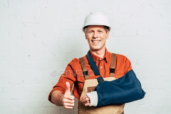 repairman with arm bandage standing and showing thumbing up on white textured background / Photodune, Misc