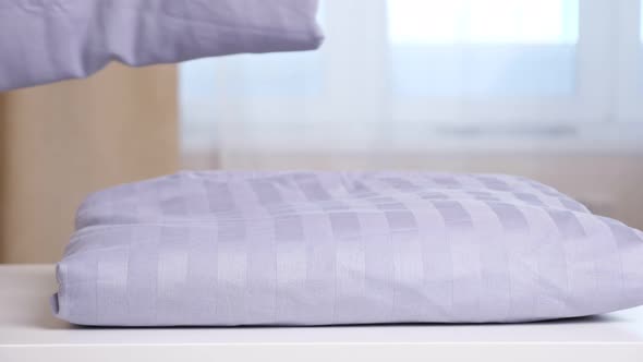 Woman Puts Purple Clean Linen Bedding Set in Stack on Table