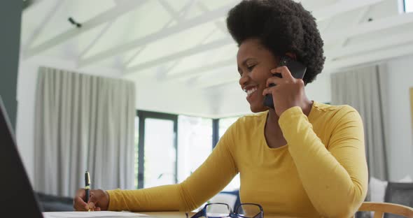 Happy african american woman sitting at table talking on smartphone smartphone