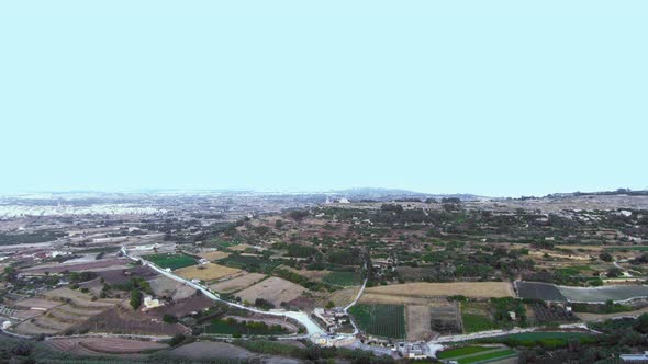 Aerial drone footage flying towards the Verdala Palace with patchwork countryside below of fields fo