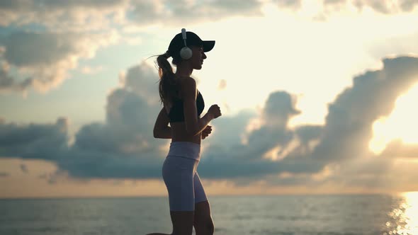 A Young Woman Runner is Listening to Music in Earphones and Training By a Sea