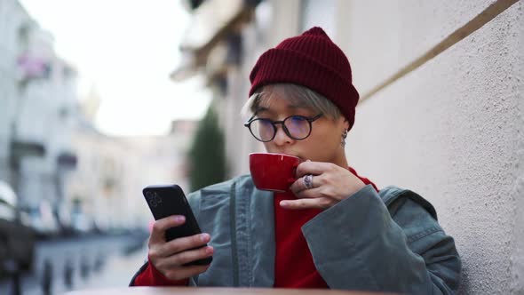 Confident Asian guy drinking coffee and looking at the phone