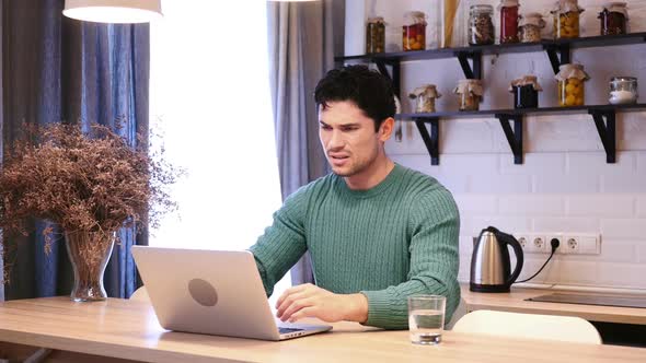 Depressed Man Upset By Loss Working on Laptop Sitting in Kitchen