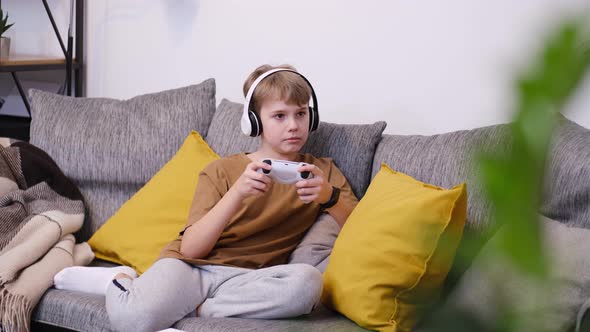 Boy Teenager Playing Video Game with Joystick Sitting on Sofa