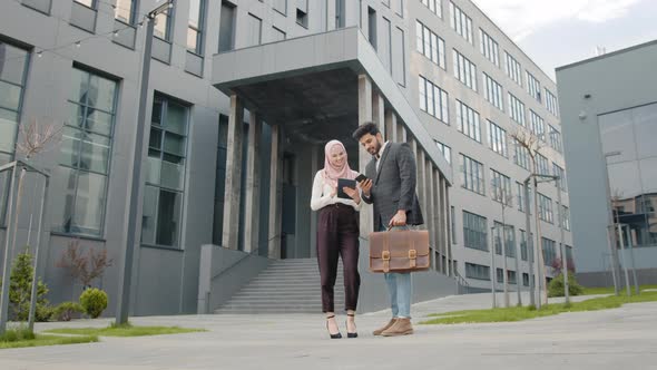 Muslim Businessman in Suit Showing Something on Smartphone to His Female