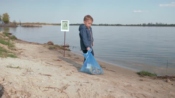 Stop Pollution, Cute Boy Pulls Heavy Bag of Trash on Pointing Sign on River Beach After Cleaning Up