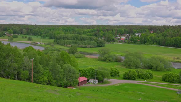 Amazing top view on green fields between green forest trees and flowing river under blue sky.