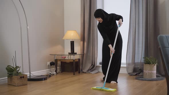 Portrait of Young Muslim Lady Cleaning the Floor. Young Lady in Black Hijab Using Mop To Do