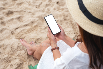 a woman holding black mobile phone with blank desktop screen while sitting on a beach chair / Photodune, Misc