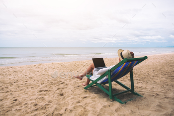 A woman using and typing on laptop computer while lying down on a beach chair / Photodune, Misc