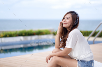 A beautiful asian woman listening to music  with headphone while sitting by swimming pool / Photodune, Misc