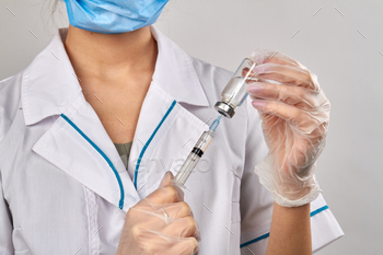 Fimale doctor injecting syringe into a vial bottle with medicine. / Photodune, Misc