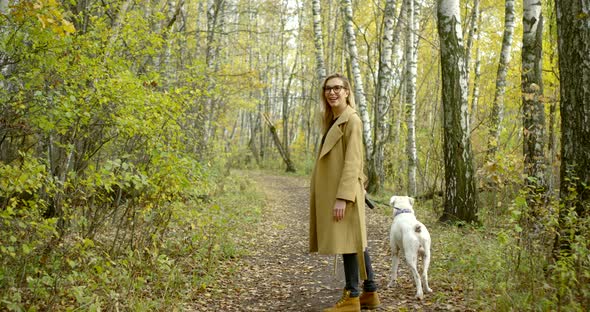 Young Blonde Girl with Glasses and a Coat, Shoes. She Smiles, Walks on the Forest More Often with