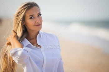 A girl with long hair in a bluish swimsuit and a shirt goes through her hair on the seashore / Photodune, Misc