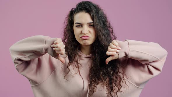 Displeased Young Woman Showing Thumbsdown Hand Gesture and Frowning on Pink Background