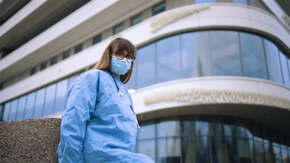 Tired Female Surgeon in Glasses and Medical Face Mask Looking at You Near Hospital