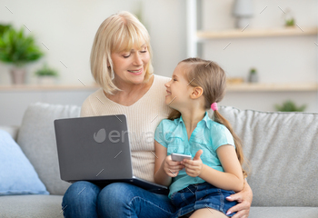 Happy mature woman and granddaughter using laptop and cell phone / Photodune, Misc