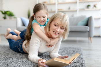 Happy mature woman and granddaughter reading book / Photodune, Misc