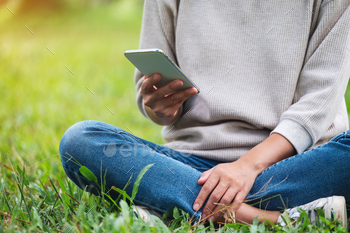 Closeup image of a young woman holding and using mobile phone in the park / Photodune, Misc