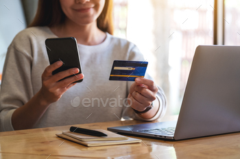 Closeup image of a woman holding credit card while using smart phone and laptop in office / Photodune, Misc