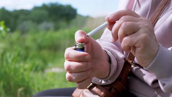 Female is Trying to Light a Cigarette with a Lighter Sitting in Nature on Sun