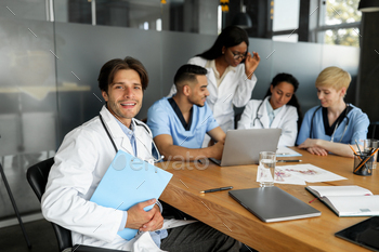 Handsome doctor smiling at camera while having brainstorming with colleagues / Photodune, Misc