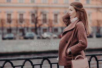 Beautiful woman dressed in stylish coat, keeps hand in pocket, focused into distance / Photodune, Misc