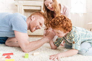 side view of father and son playing arm wrestling with mother near by, family fun at home concept / Photodune, Misc