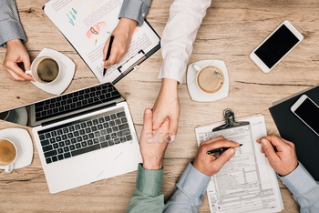 Top view of business people handshaking by gadgets, documents and coffee on table / Photodune, Misc