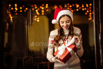 surprised young woman in warm sweater and santa hat opening gift box / Photodune, Misc