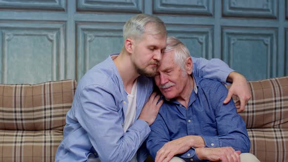 Young Man Asking for Apologizes to Offended Stressed Elderly Senior Father Sitting Together on Couch