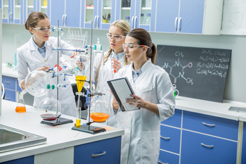Three female scientists in protective goggles making experiment in chemical laboratory / Photodune, Misc
