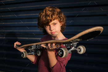 Boy examining skateboard against blue wall / Photodune, Misc