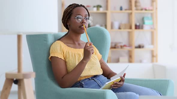 African Woman with Braids Thinking and Writing in Notebook with Pencil