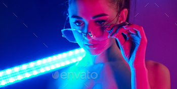 Holds neon lighting stick. Fashionable young woman standing in the studio / Photodune, Misc
