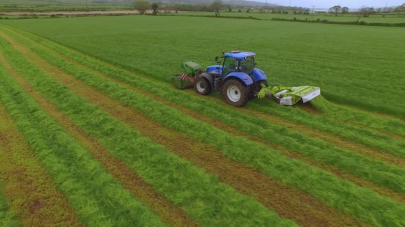 Aerial view of a tractor cutting the grass in a large green field.