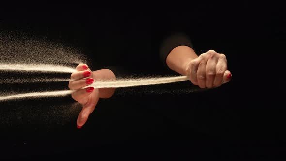 Stream of Dry Sand Pours Into Palm of Woman and is Spilling Through Her Fingers on Black Background