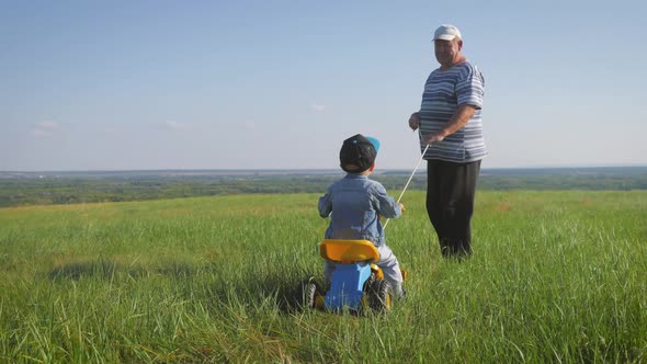 Senior Man Grandfather Teaches His Grandson To Ride a Bike in Nature. He Pulls It By the Rope, the