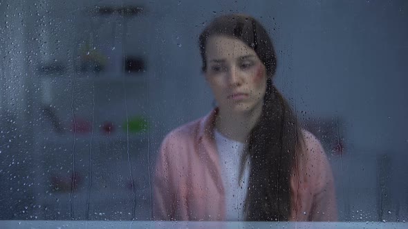 Depressed Woman With Wounded Face Sitting Behind Rainy Window, Assault