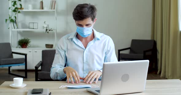 Funny Comical Caucasian Male Freelancer Disinfecting Computer with Spray, Sitting in Cabinet at Desk