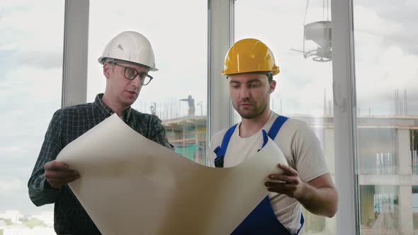 Engineer and Construction Worker Discuss a Blueprint alt