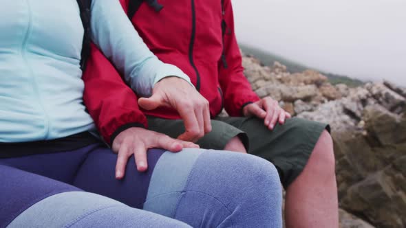 Mid section of senior hiker couple with backpacks sitting on the rocks