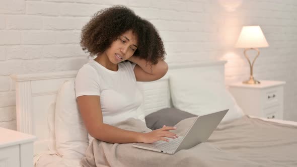 Young African Woman with Laptop Having Neck Pain in Bed