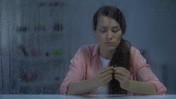 Disappointed Female Holding Engagement Ring Behind Rainy Window, Divorce Concept