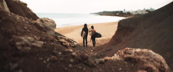 Two surfers standing in front of a rocky mountain with their boards staring at the waves