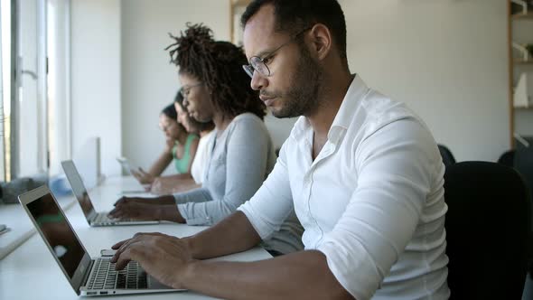 Thoughtful Man in Eyeglasses Typing on Laptop at Office