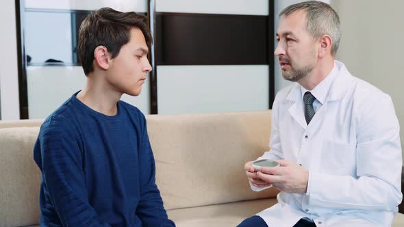 An otolaryngologist explains to a young man in behind-the-ear hearing aids how they work