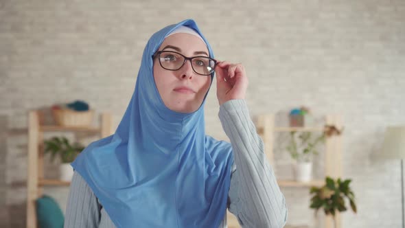 Young Muslim Woman in a Hijab with Poor Eyesight Puts on Glasses for Vision and Looks Around